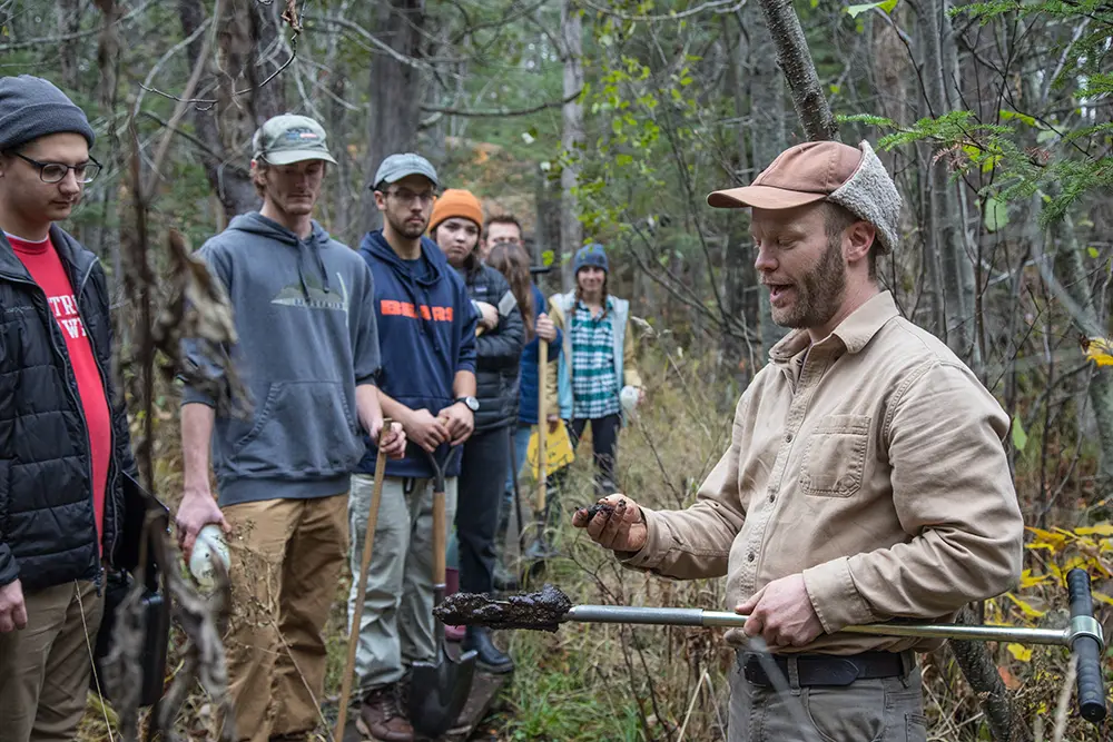 Professor Matthew Van Grinsven in the woods teaching students soil field work.