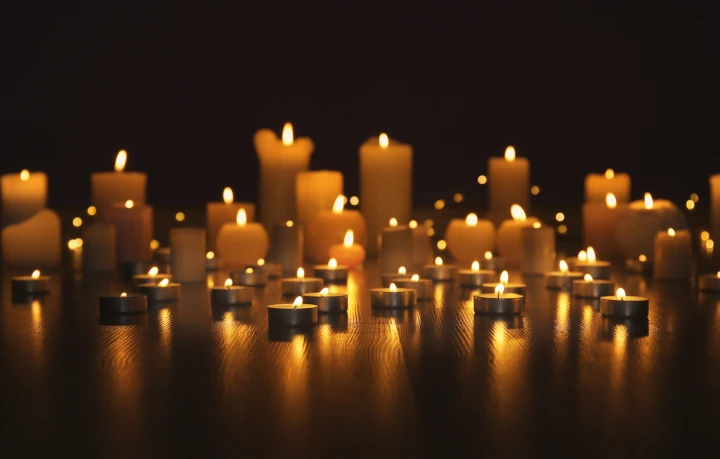 Various sizes of memorial candles, lit on a wooden shelf.