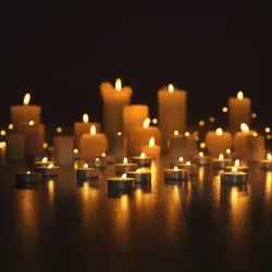 Various sizes of memorial candles, lit on a wooden shelf.
