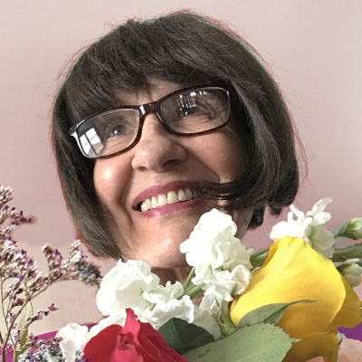 Beverly Matherne smiling with dark bobbed hair and glasses, holding colorful flowers.