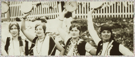 Four Italian women standing side by side holding tambourines above their heads.